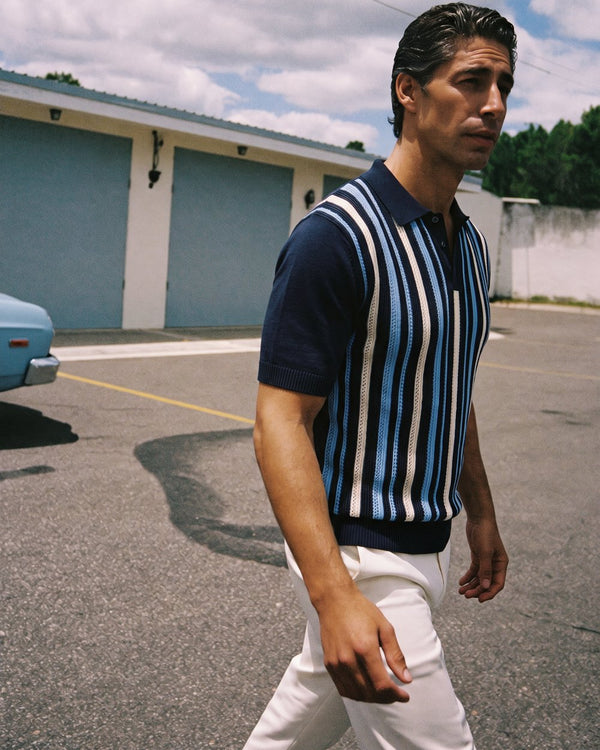 A man in a striped knit polo crossing a motel parking lot