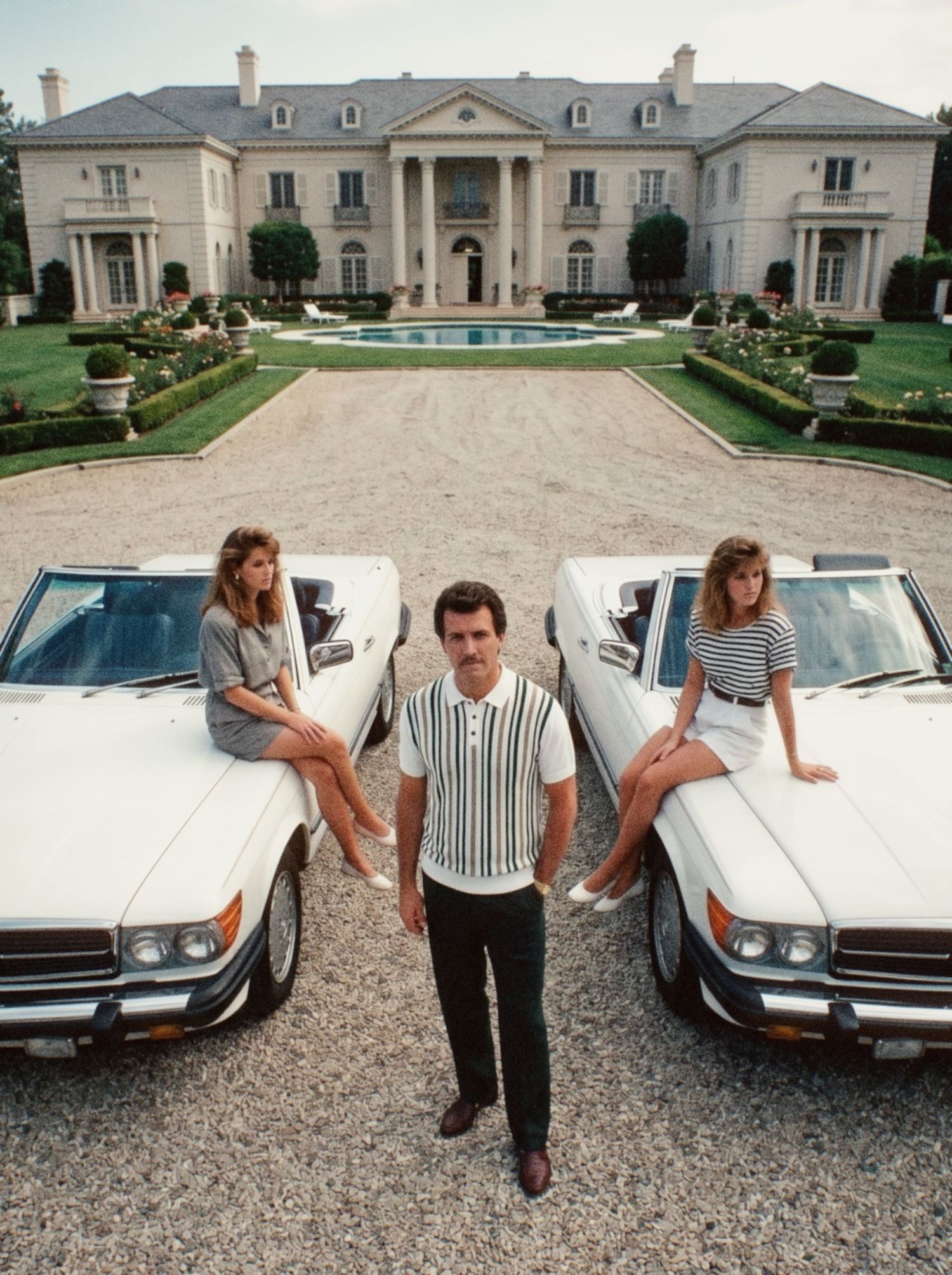 A man in a knit polo in front of a country house